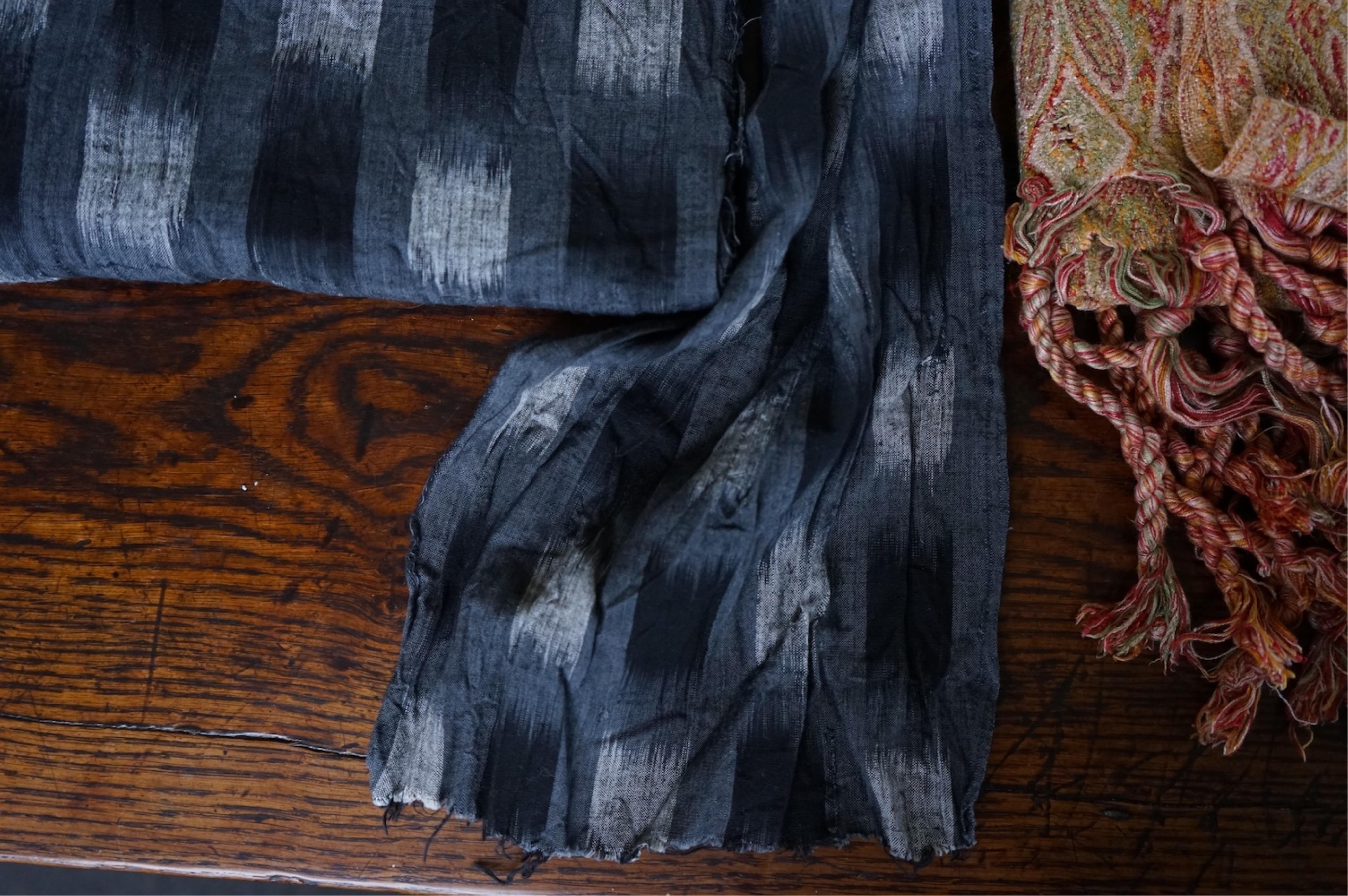 A long narrow length of grey Ikat woven fabric, a roll of Indian mirrored edging, a geometric batik printed length and a woven paisley ‘style’ tasselled stole. (4). Batik 392cm long x 108cm wide., Condition - good, all a